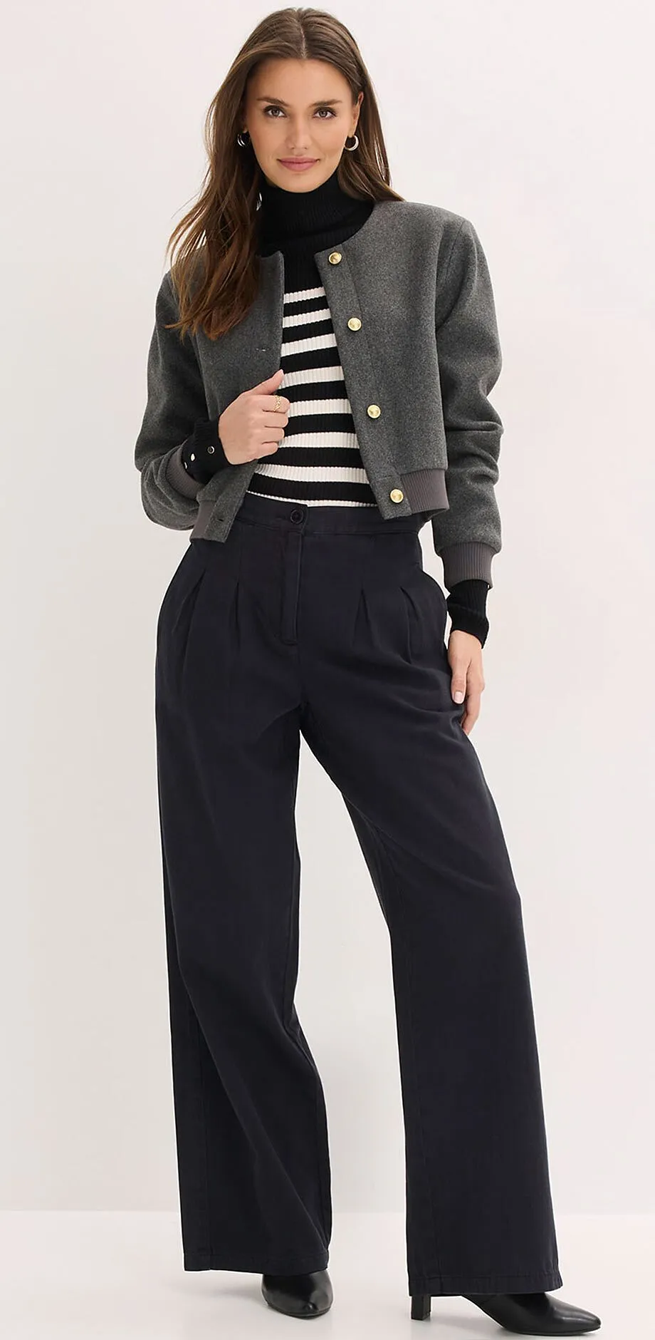 Graue Jacke, gestreifter Pullover und weite schwarze Hose.