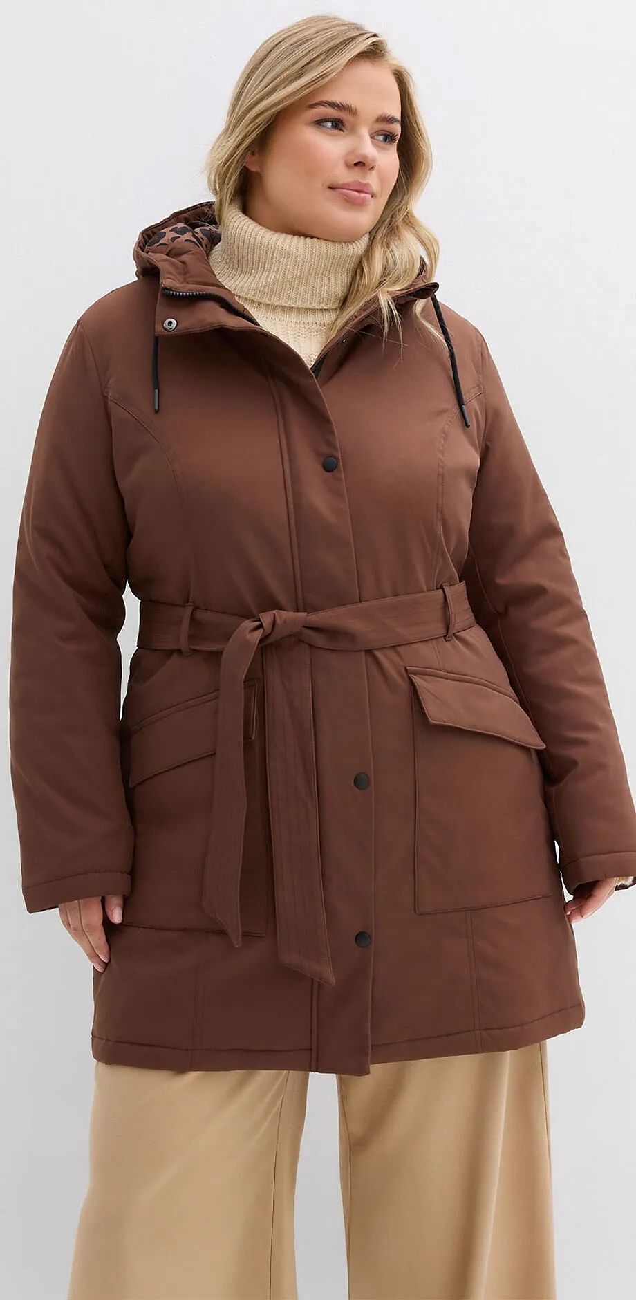 Manteau marron avec ceinture, associ&eacute; &agrave; un pull &agrave; col roul&eacute; beige et un pantalon clair.