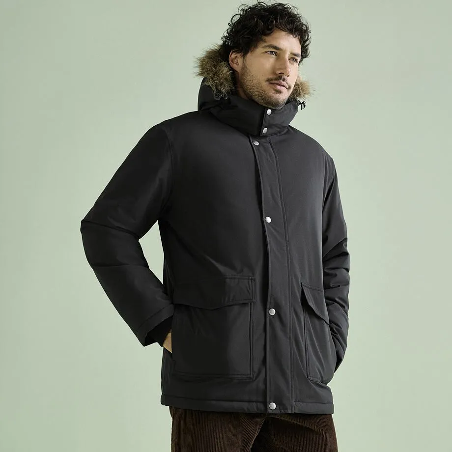 Mann tr&auml;gt schwarzen Winterparka mit Pelzkapuze und braune Cordhose.