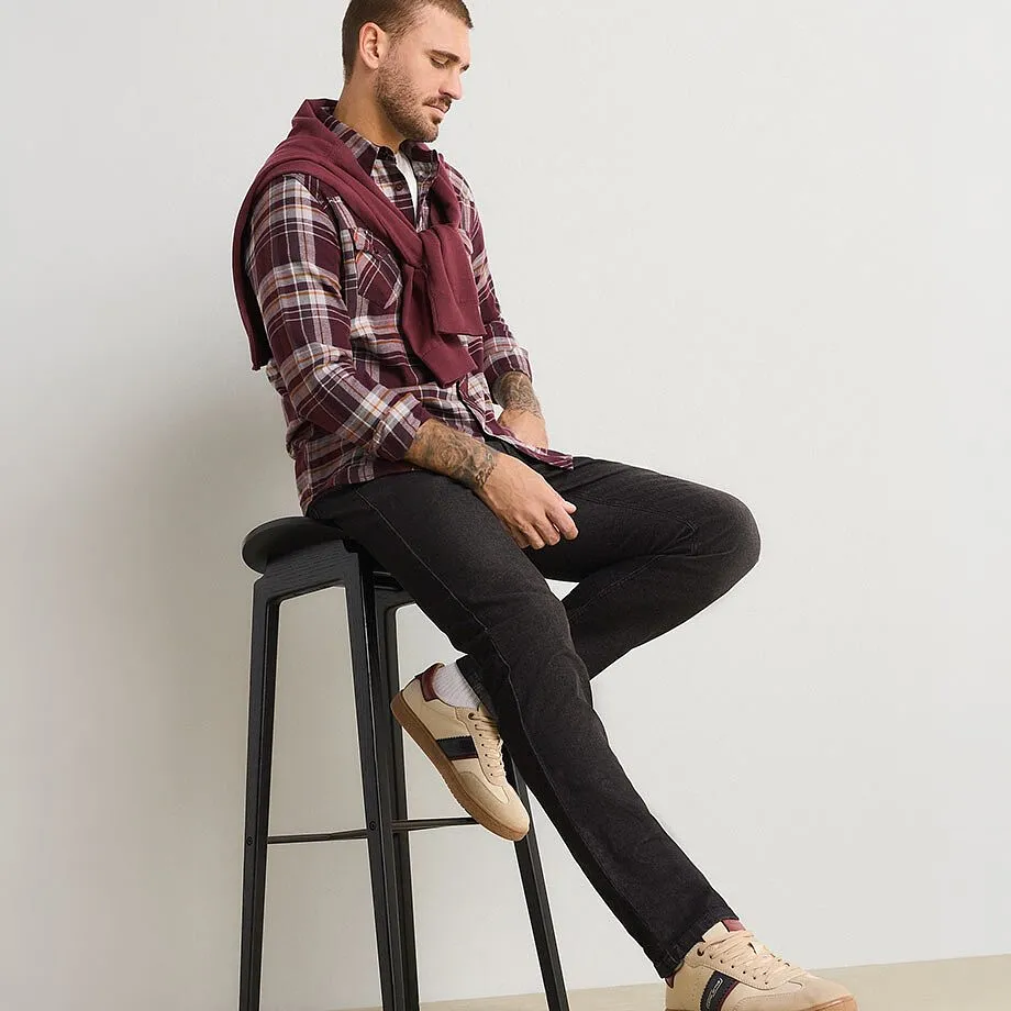Der Mann tr&auml;gt ein kariertes Hemd, dunkle Jeans, beige Turnschuhe und einen weinroten Pullover.