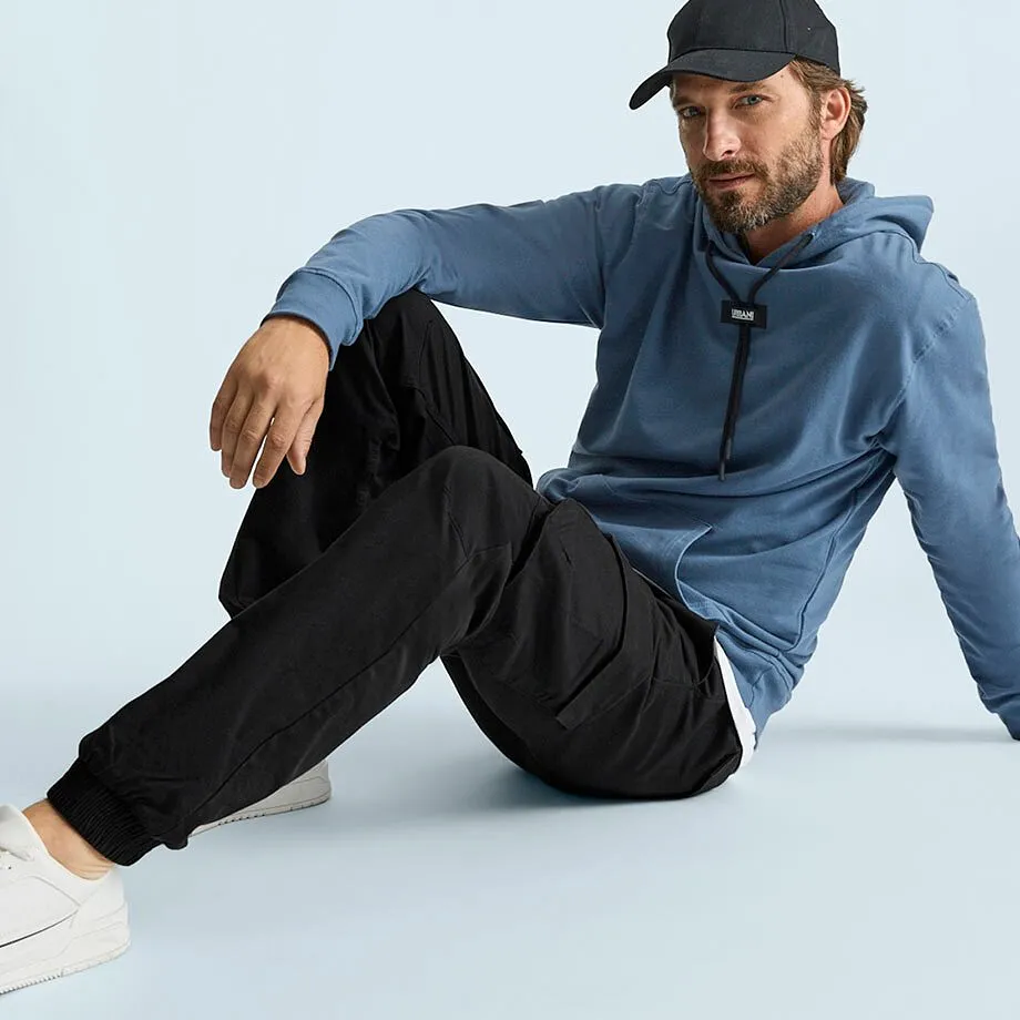 Der Mann tr&auml;gt einen blauen Kapuzenpullover, schwarze Cargohose, wei&szlig;e Sneaker und Kappe.