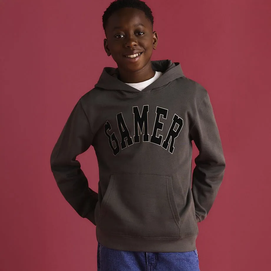Hoodie in Grau und Schwarz mit "Gamer" Aufdruck, dazu blaue Jeans.