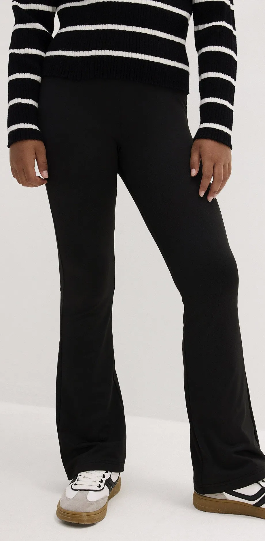 Schwarze Leggings mit ausgestelltem Bein, dazu weiss-schwarze Sneaker und ein Streifenpullover