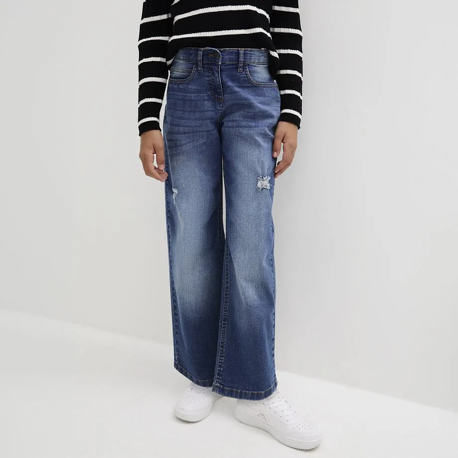 Das Kind tr&auml;gt gestreiftes Langarmshirt, blaue Schlagjeans und wei&szlig;e Sneaker.