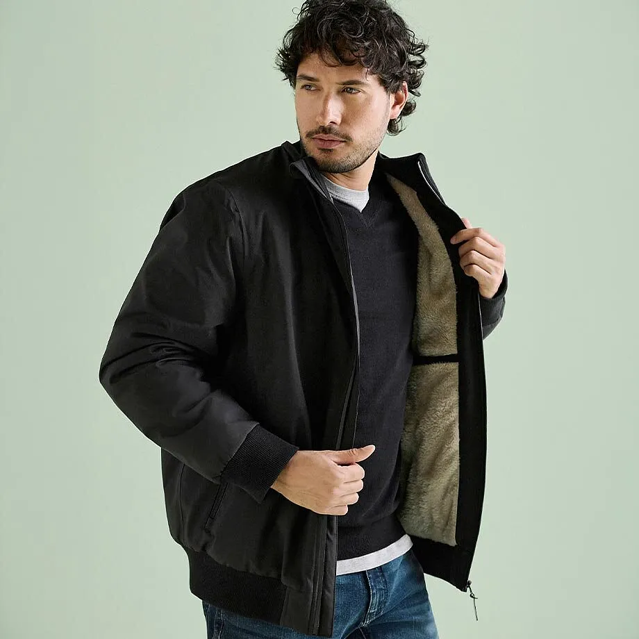 Schwarze Bomberjacke mit flauschigem Futter, dunkler Pullover und Jeans.