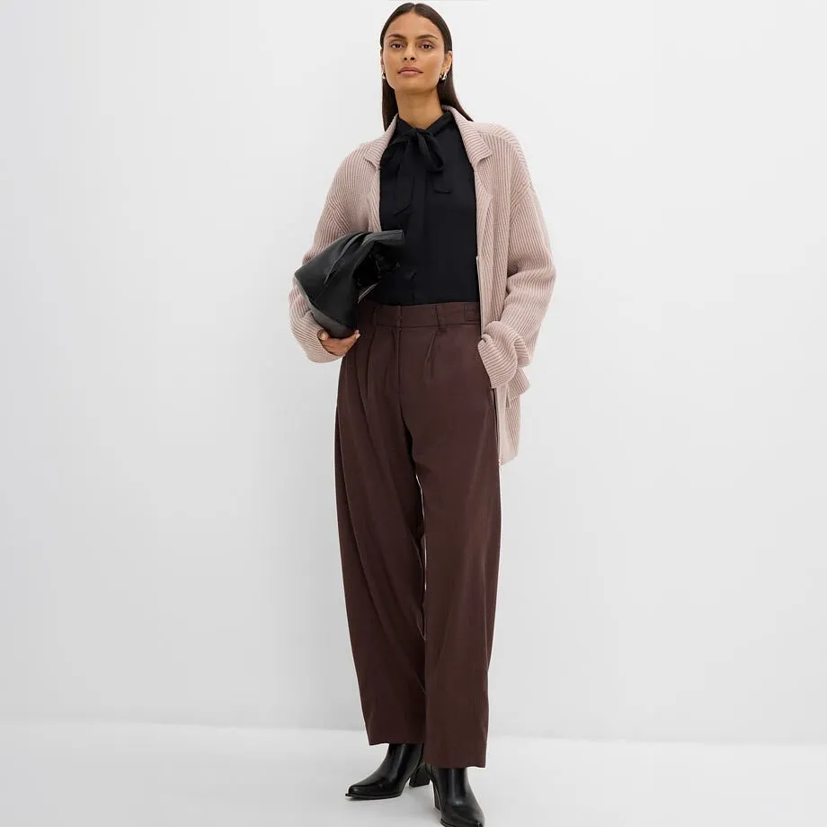 Femme v&ecirc;tue d'un chemisier noir, un cardigan en maille beige, un pantalon marron et des bottines noires.