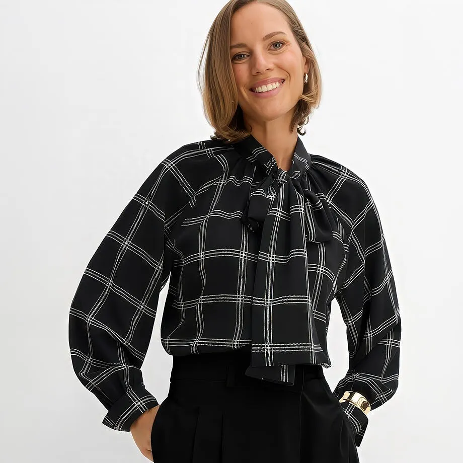 Blouse noire &eacute;l&eacute;gante &agrave; carreaux et n&oelig;ud, pantalon noir, bracelet de couleur dor&eacute;e.
