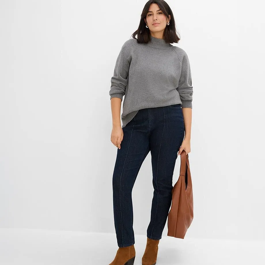 Pull gris &agrave; col montant, jean fonc&eacute; avec coutures, bottines et sac marron.