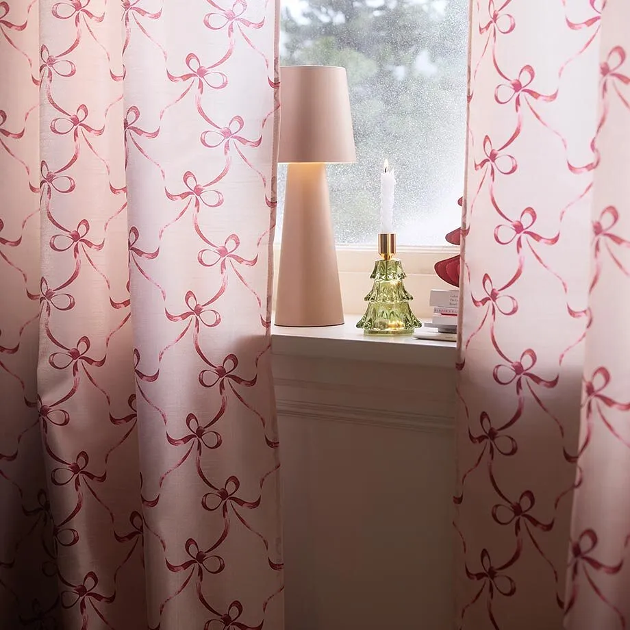 Des rideaux roses &agrave; motifs petits n&oelig;uds d&eacute;corent la fen&ecirc;tre ainsi qu'une lampe et une bougie.