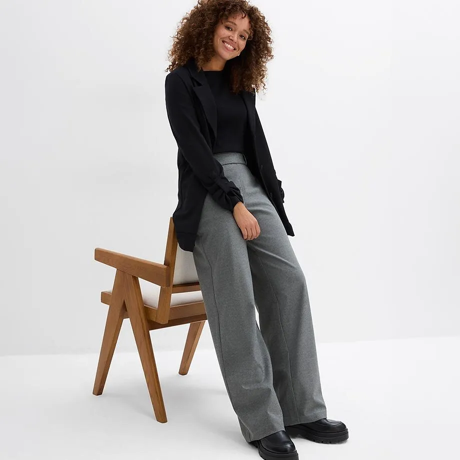 Haut noir, blazer, pantalon gris de coupe large et chaussures noires robustes.