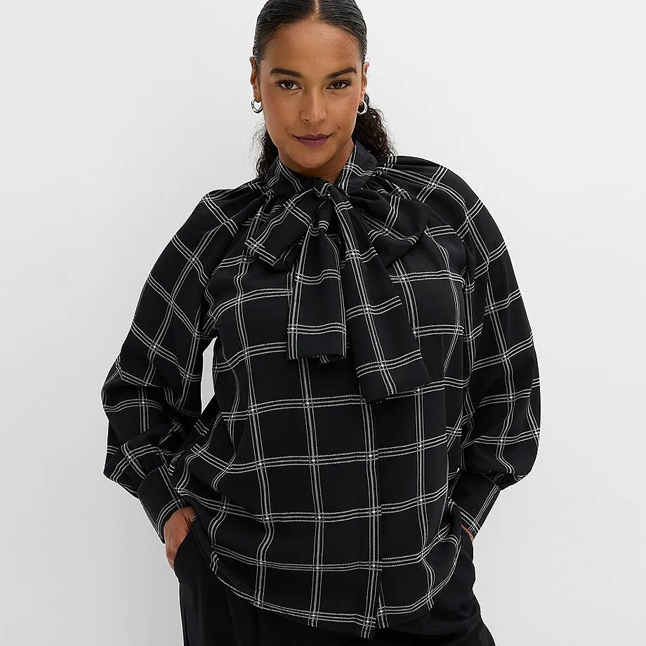 Elegante schwarze Bluse mit wei&szlig;em Karomuster und gro&szlig;er Halsschleife, dazu schwarze Hose.