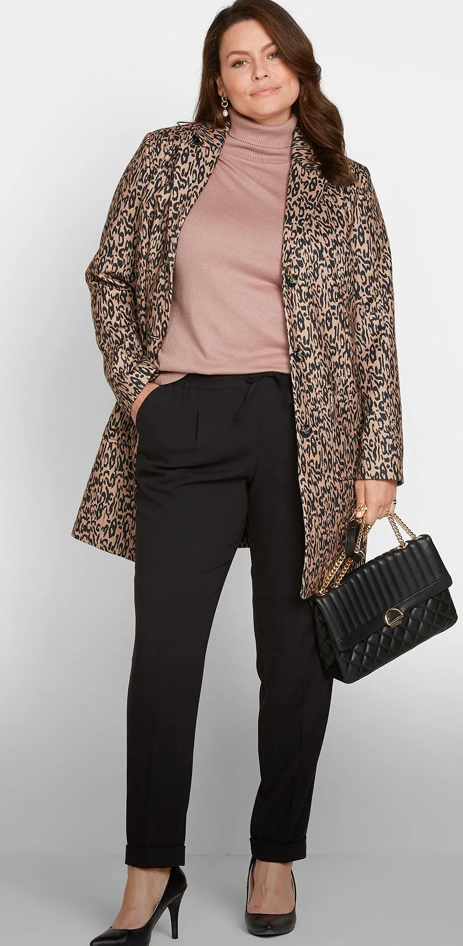 Stilvoller gemusterter Mantel, rosafarbener Pullover, schwarze Hose, Pumps und Handtasche.