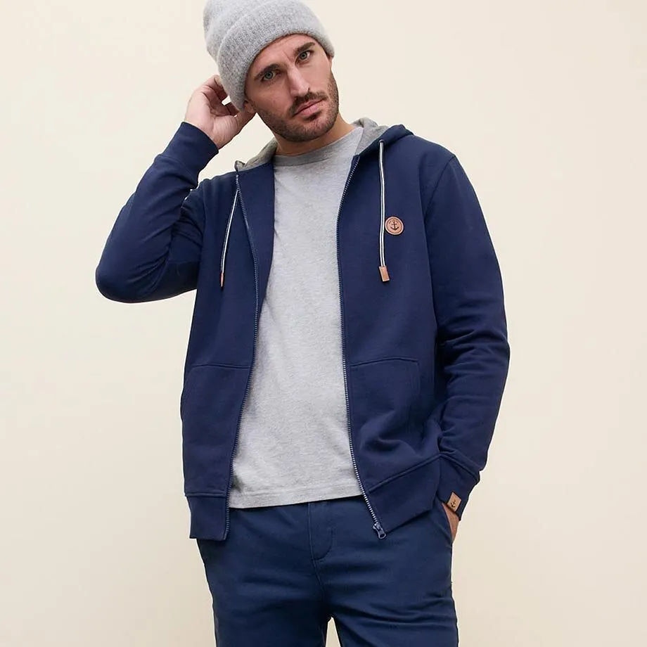 L&auml;ssiger Look mit blauer Kapuzenjacke, grauer M&uuml;tze und hellem Pullover.