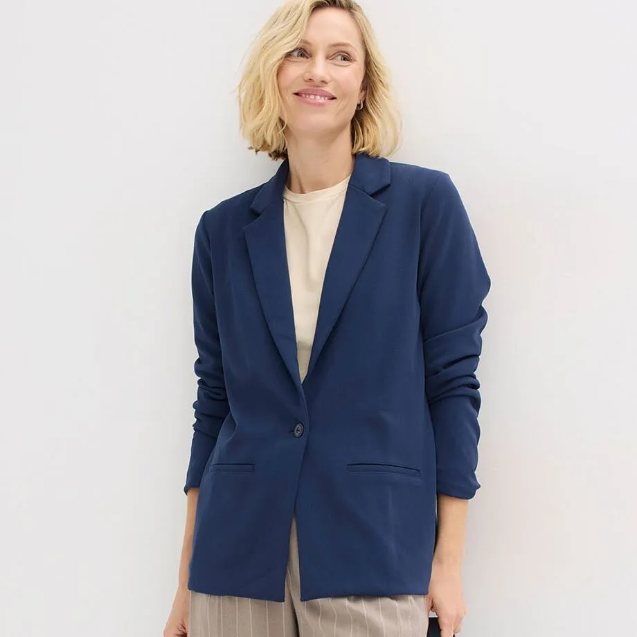 Blazer bleu associ&eacute; &agrave; un pull couleur cr&egrave;me et un pantalon beige.