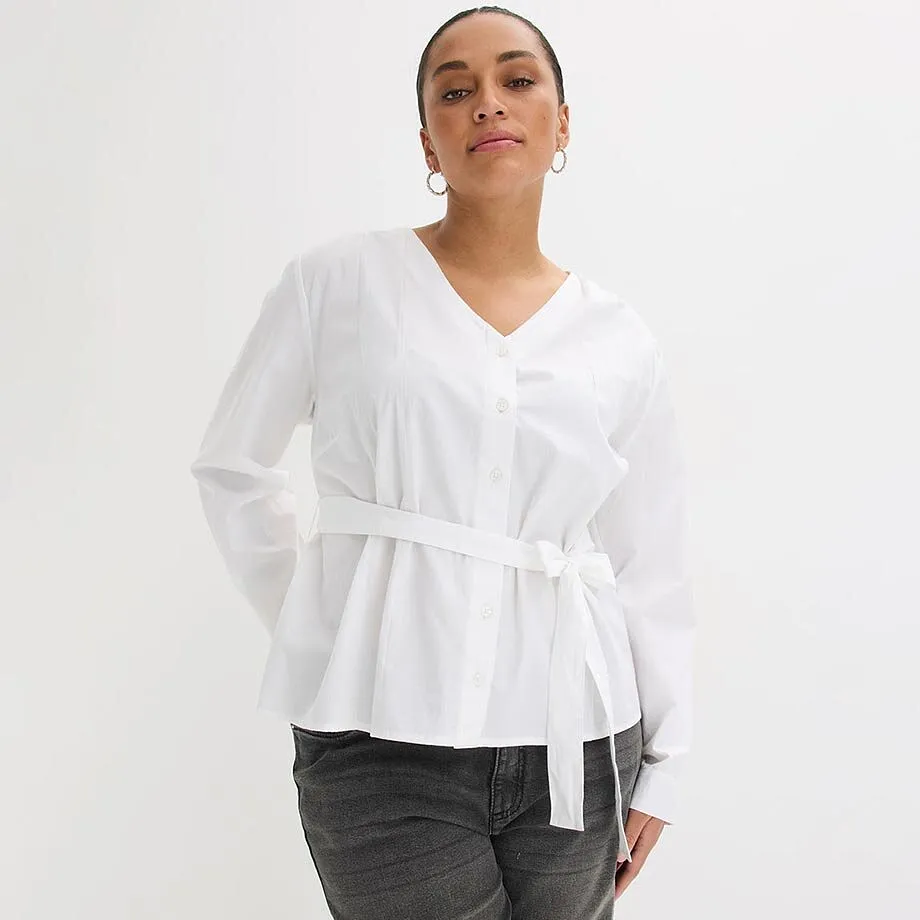 Chemisier blanc avec d&eacute;collet&eacute; en V et lien-ceinture, associ&eacute; &agrave; un jean fonc&eacute;.