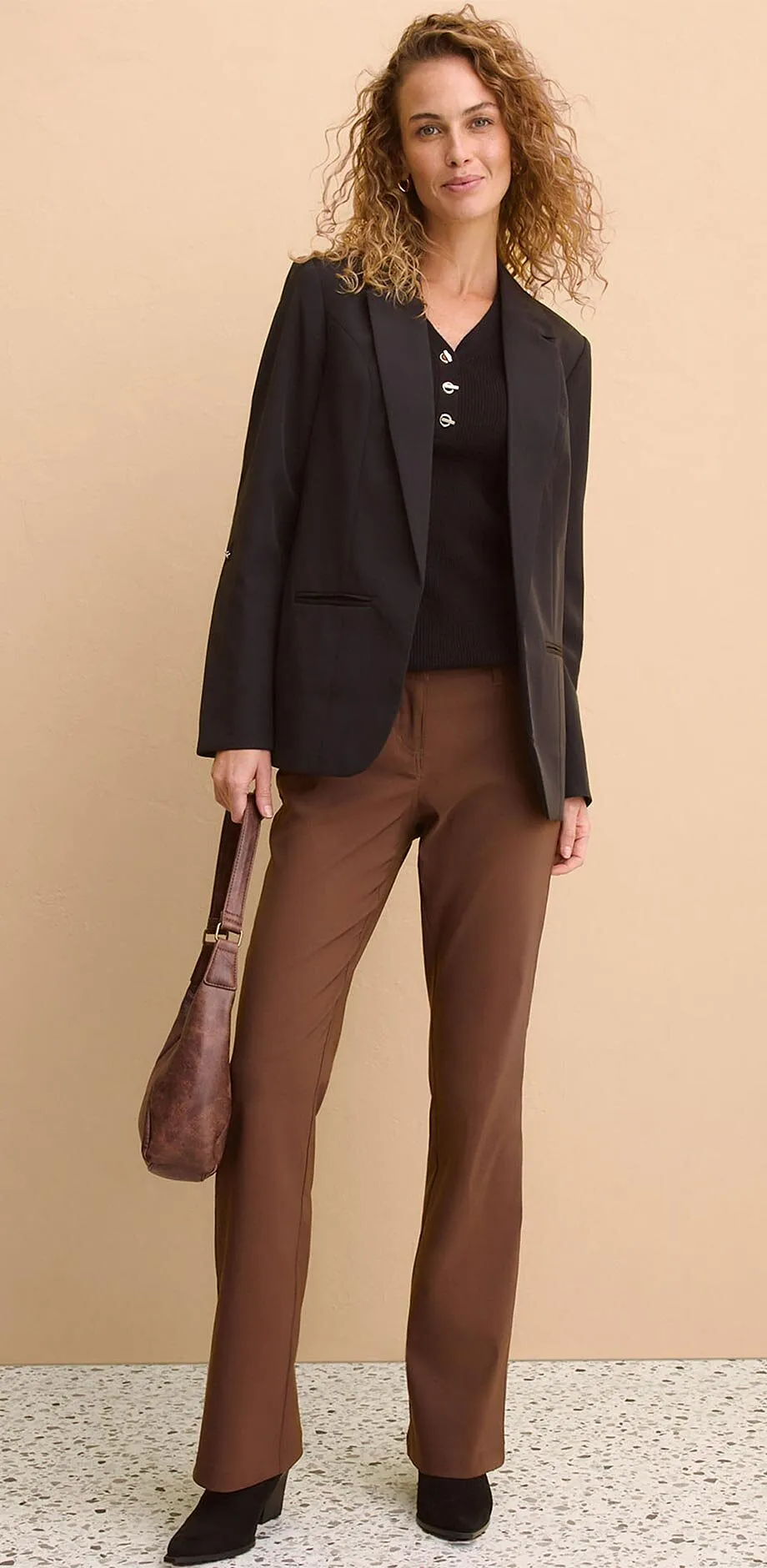 Blazer noir par dessus un top fonc&eacute;, associ&eacute; &agrave; un pantalon marron.